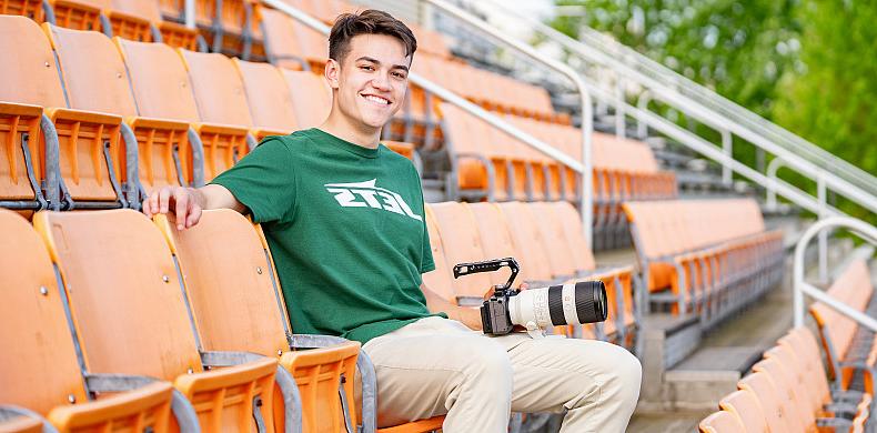 一名身穿绿色喷气机队t恤的男子坐在体育场的橙色座位上.